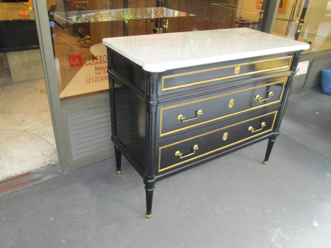 Directoire style ebonized commode with marble top on fluted legs ending on brass sabots.