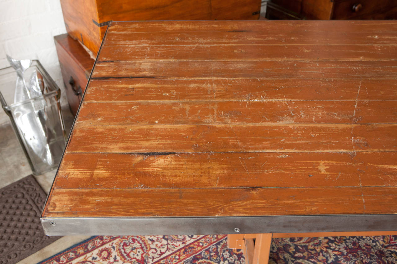 A long dining table that was originally a painted work table from Ghent, Belgium. This rustic table with distressed table top has a steel border that has been added at a later date. The interesting angled legs give the piece a really unique blend of