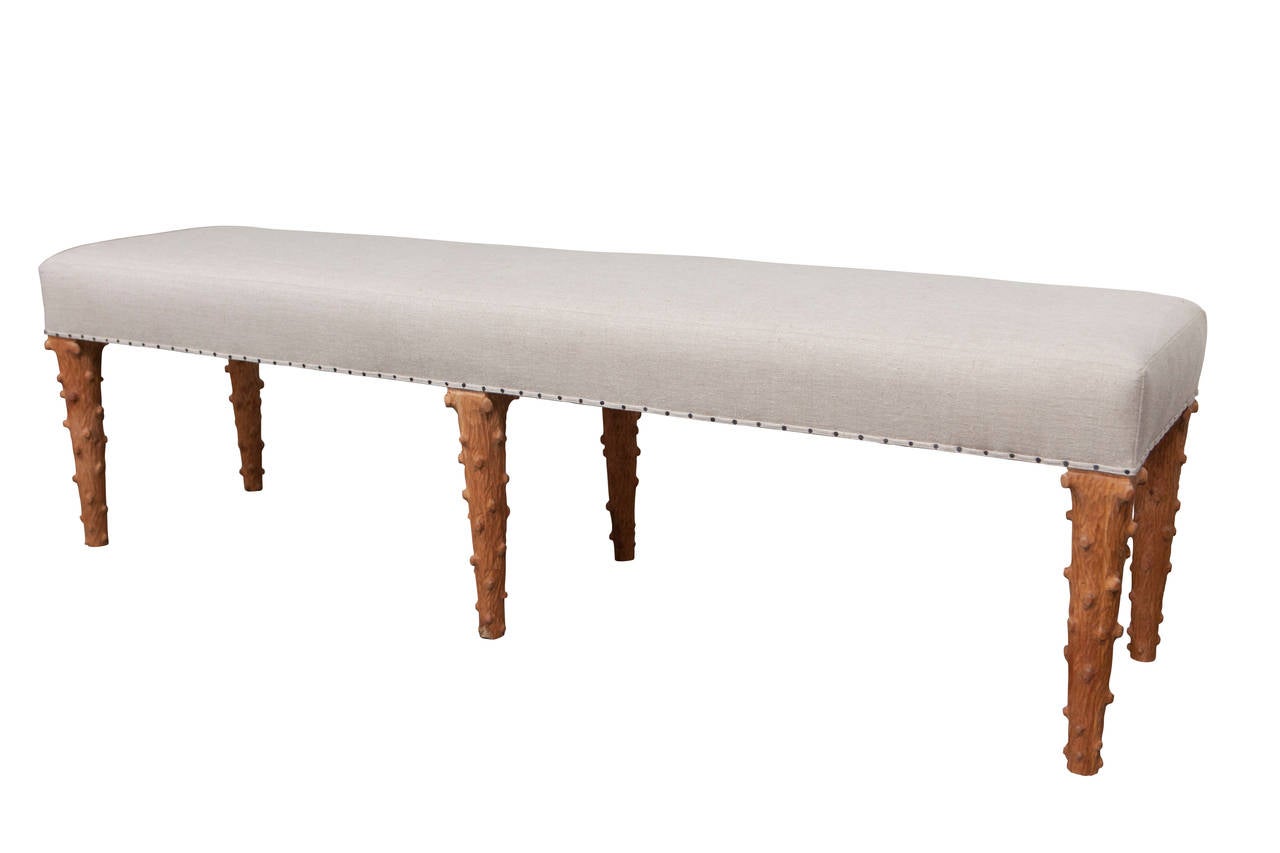 This bench was designed and produced using the skills of master craftsmen and upholsterers. It has six hand-carved tree stump legs and can be upholstered in your fabrics. It is shown here in linen. It is shown with nailheads.