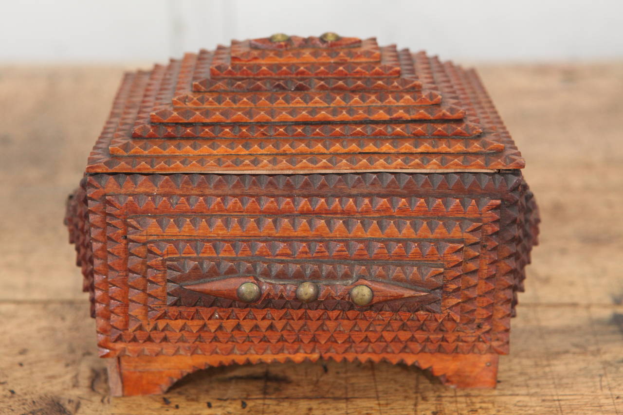 This spectacular example of an american tramp art box that stands on raised legs with multiple geometric layers of hand cut cigar box wood. The box has the added interest of brass tacks as decorative details. The interior has the original fabric