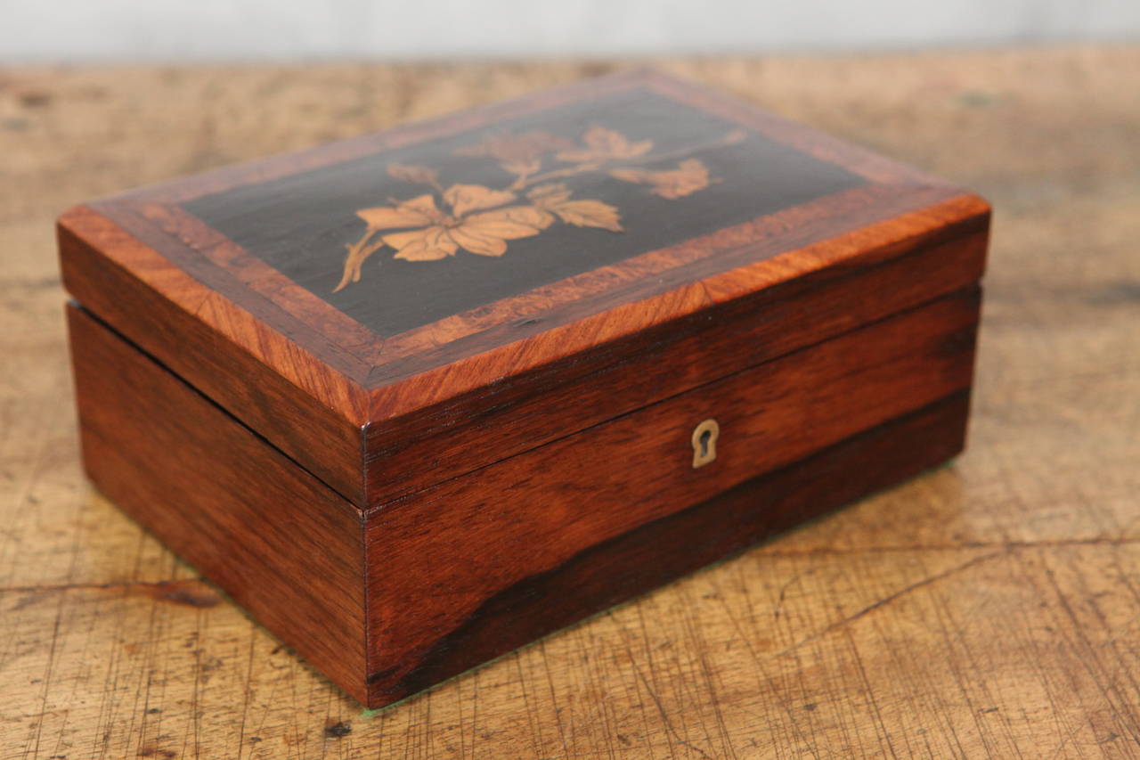 This nice oak box has an lovely finish having a  lid that features floral marquetry with burled and straight cut walnut banding as a border. the box has brass hinges, lock and escutcheon. The box is lined with Japanese block print paper in a red and