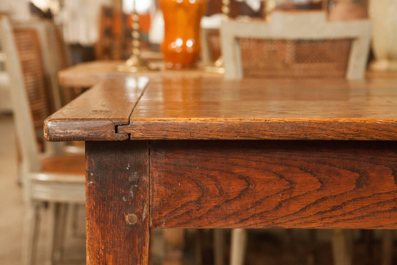 This is a simple farm table with traditional tapered legs and one drawer at one end of the table with turned wooden knob. The top has five boards with bread boards at each end. The table is well-made and structurally sound with an rugged patina that