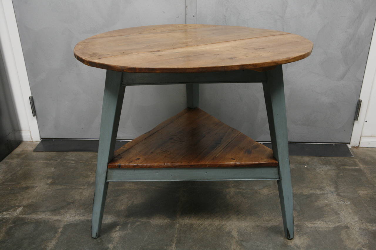 This interesting cricket table is a reconstructed piece we believe was made in England in the 1980s with an older aged wood tabletop and newer pine legs and triangular shelf. The blue painted legs give this piece a unique versatility for a variety