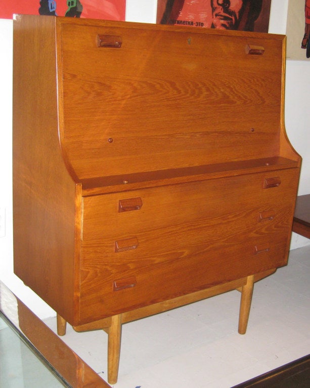 Three-drawer solid teak chest with drop-front secretary on solid birch base. Brass key and hardware. Stamped 