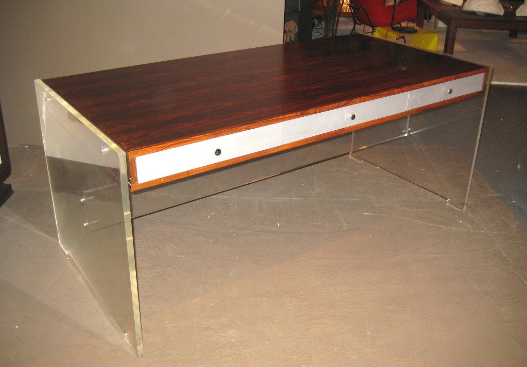 Rare and collectible lucite and rosewood desk. Lucite slab sides with beautifully grained Rosewood case, aluminum spacers, painted drawers, and nickeled brass pulls. An unusual and modern mix of materials for danish design predates the American