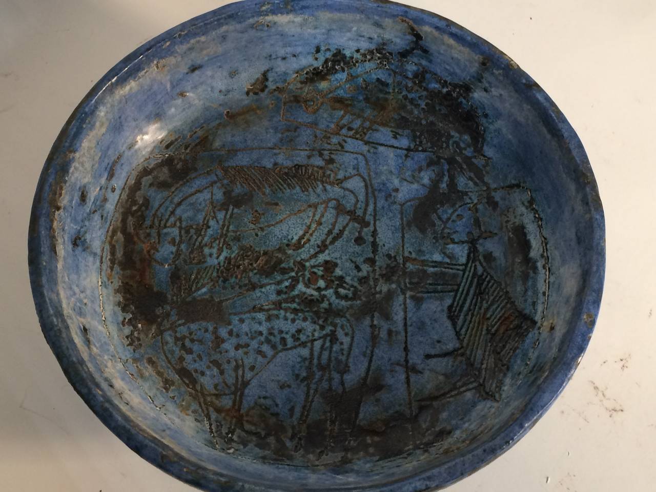 Mottled blue glaze ceramic bowl with Primitive sgraffito design etched over both interior and exterior. Signed J. Blin to underside.