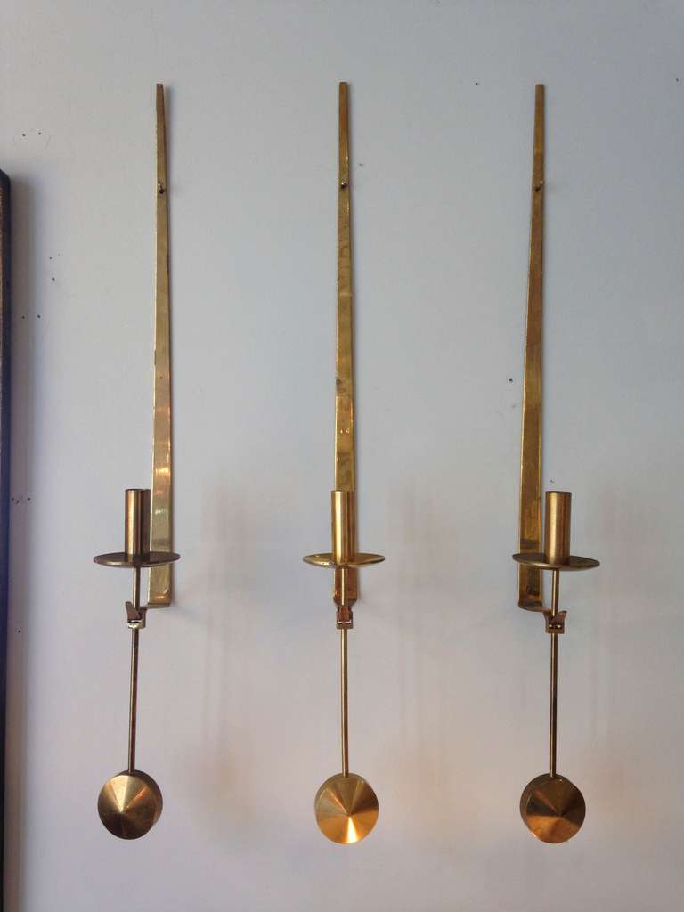 Weighted brass pendulum candlesticks hang from brass mounts. For Skultuna, Sweden.