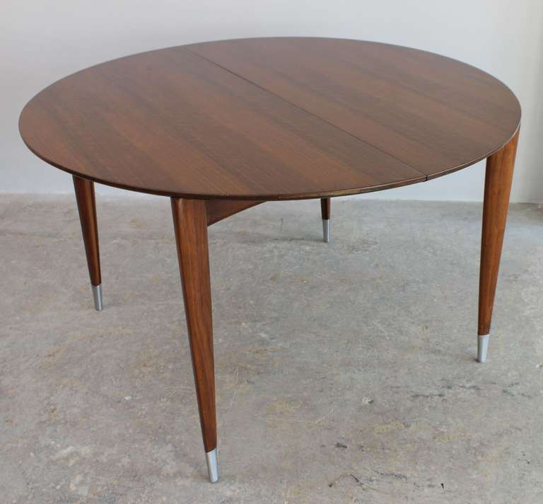 Round walnut dining table with tapered details and metal sabots. Extends to 104 inches total.

designed by Gio Ponti for Singer and Sons.

 Leaves can be ordered; please inquire.