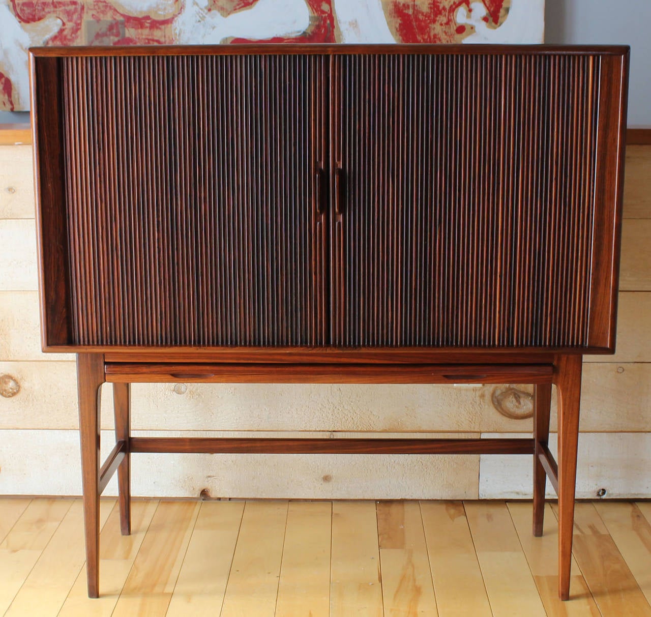 A distinctly handsome Danish rosewood bar cabinet with tambour doors and pullout plateau with black leather finish. Textured glass shelves and wine storage with rosewood bumpers; also interior lighting. Designed by Kurt Ostervig for K.P. Mobler.