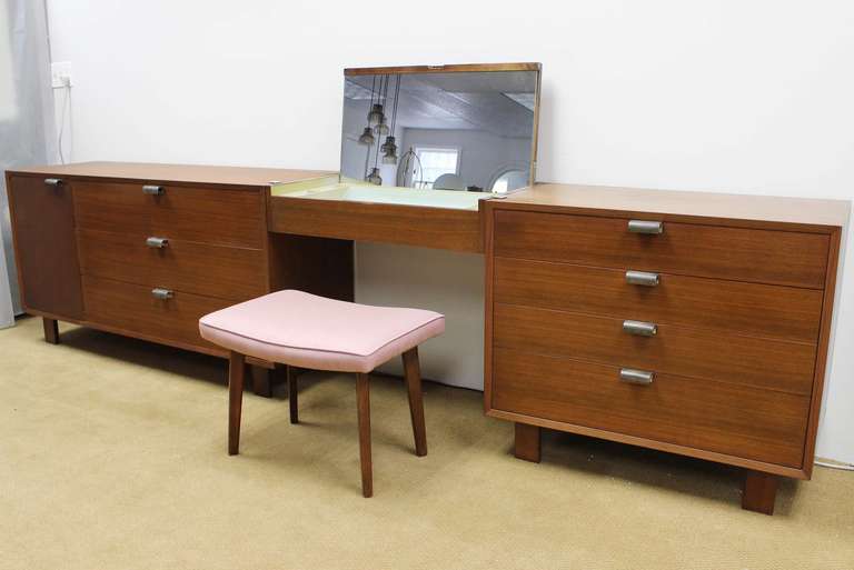 Classic walnut George Nelson dressers and mirrored vanity/bench set, for Herman Miller; labelled.

23.5 inch clearance under vanity.