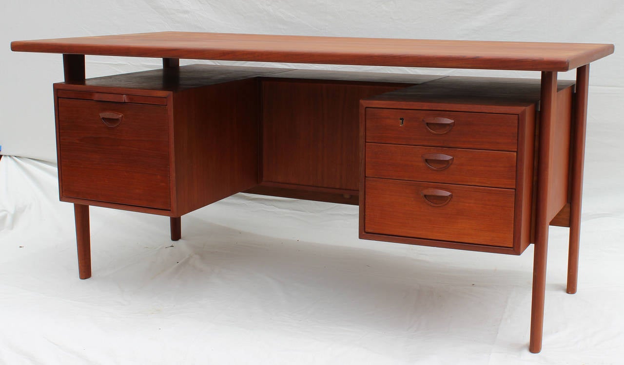 A teak executive desk with wood pulls and opposite shelving, designed by Kai Kristiansen.