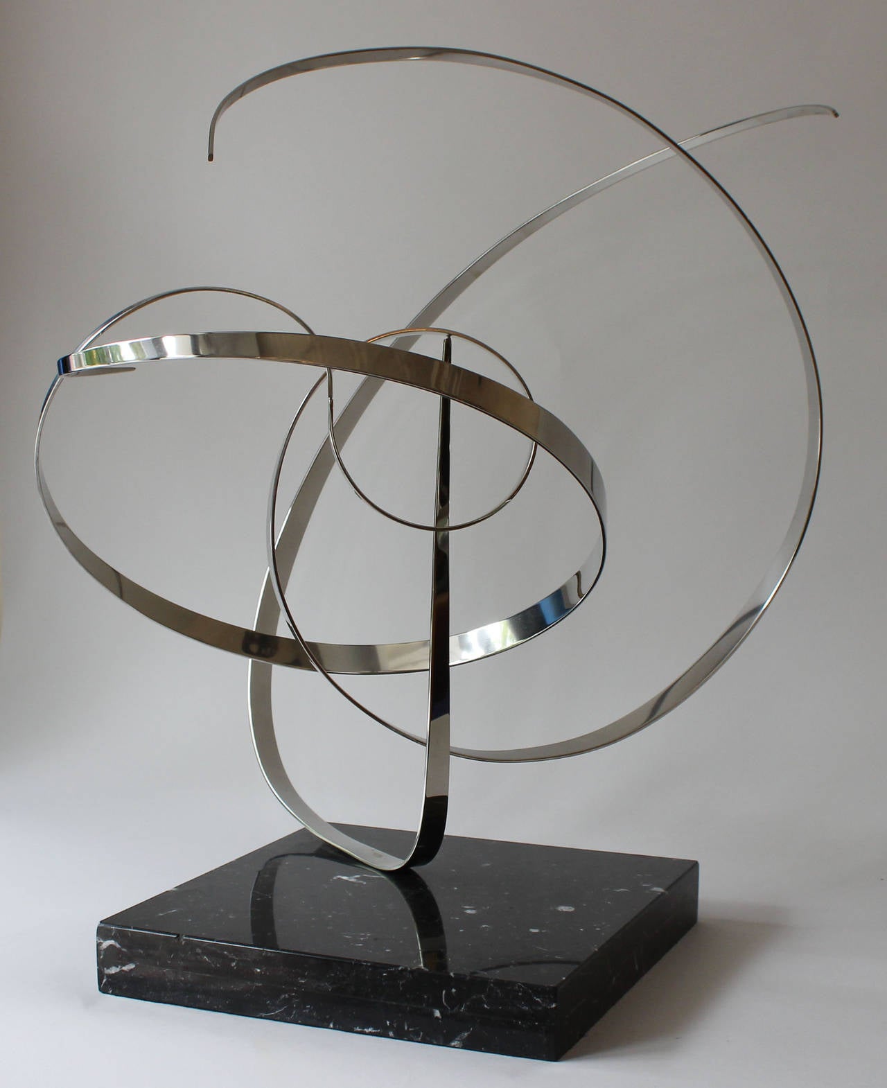 A large, kinetic sculpture on marble base, comprised of three pivot point connecting stainless steel ribbons. Rotates and adjusts with wind or light touch. By self-taught California electronic technician cum artist Michael Cutler (b1947), who began