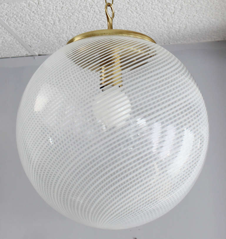 Exquisite clear murano glass globe with thin white lines and patinaed brass hardware.