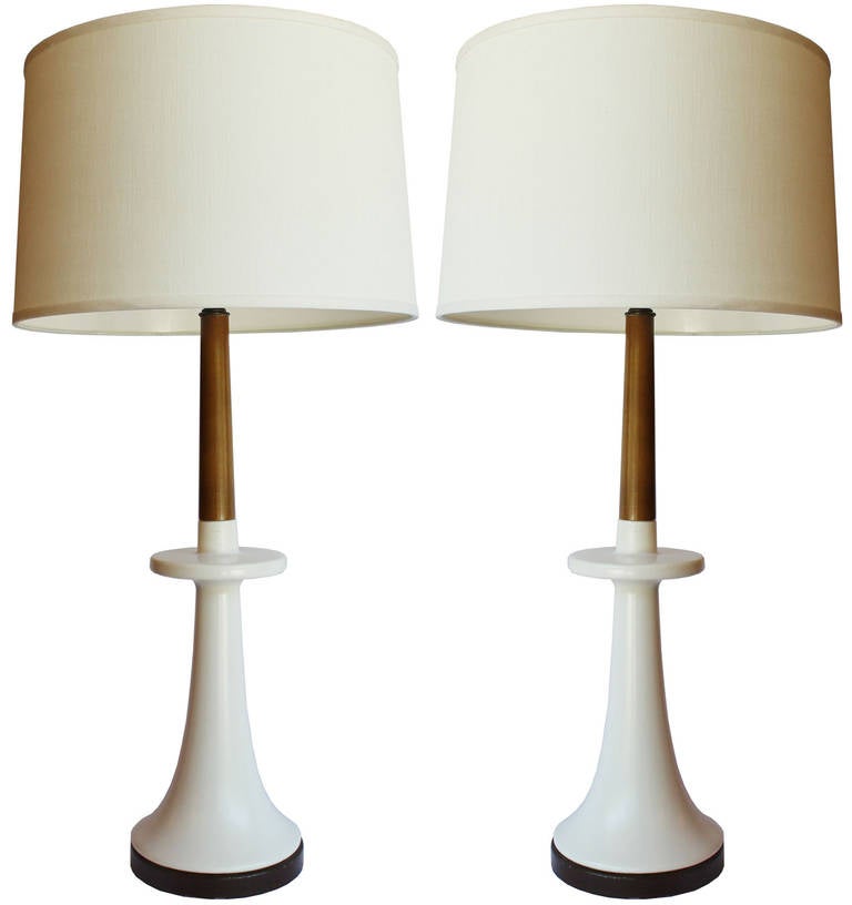 A pair of white porcelain and walnut candlestick holder lamps with metal bases and brass hardware.

shades for photo only. 30