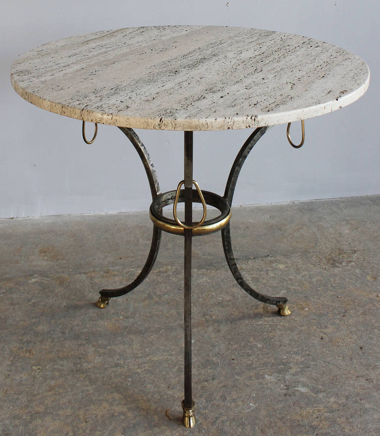 A patinaed steel and brass tripod table with travertine top.