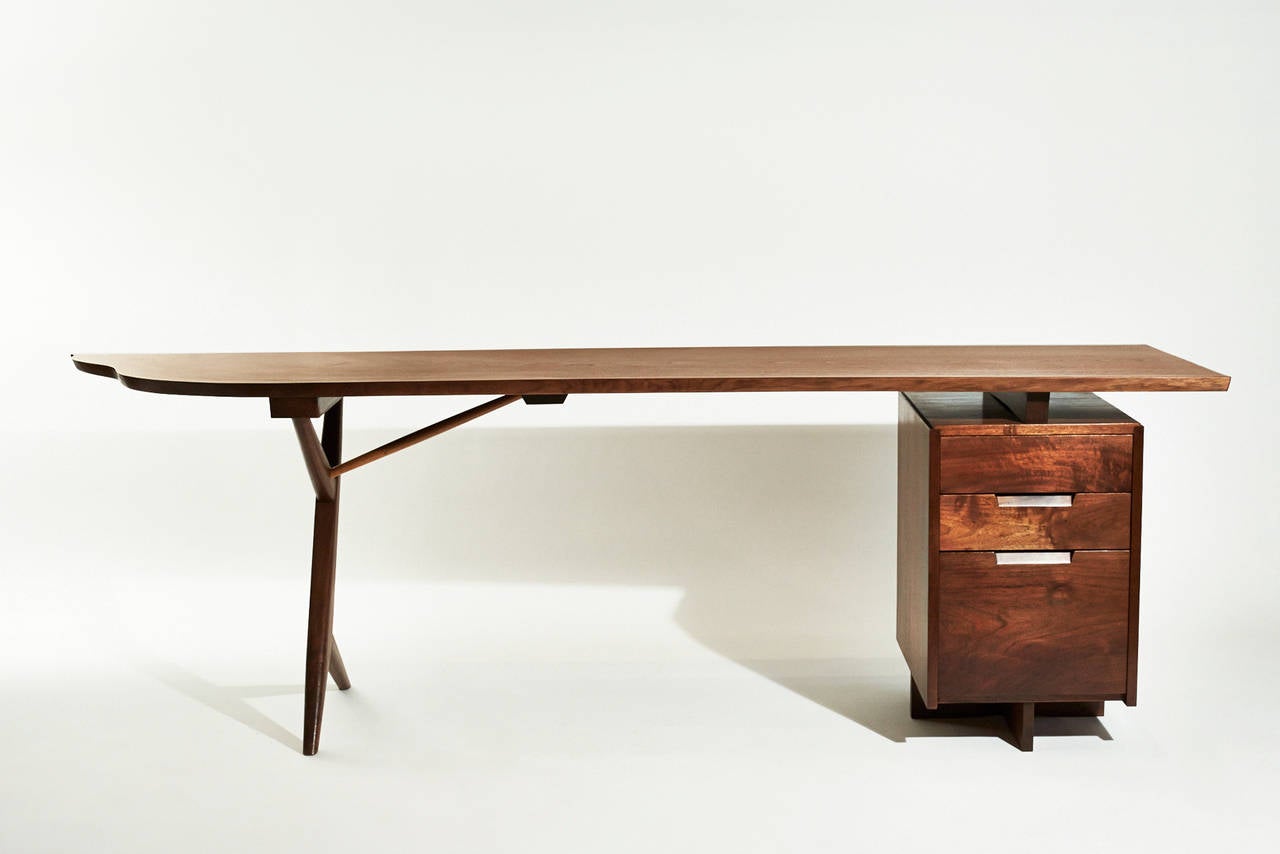 This outstanding Conoid desk by George Nakashima has a highly figured American black walnut top. On one side is an exquisite walnut case file drawer pedestal  with three drawers and a Hickory support, and  on the other is a cross legged base . The