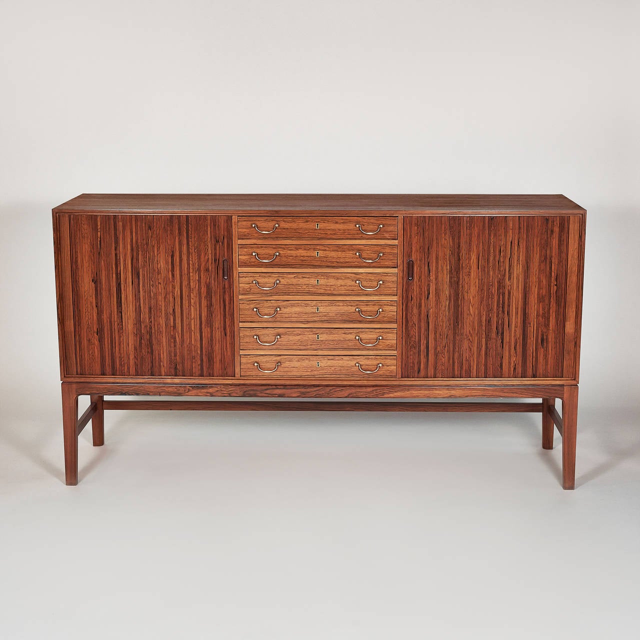 This beautiful tambour cabinet was designed by Ole Wanscher for A.J. Iversen Snedkermester. It is made from rosewood and features two tambour doors with brass fittings. The interior has three adjustable shelves and six drawers. The tambour door