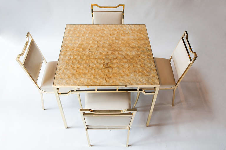 Beautiful brass table and chairs by Billy Haines, USA, circa 1950s. Table with inlaid capiz shell top. Chairs feature original cream vinyl upholstery and typical sabre style legs. Beautiful golden patina to tabletop.

Excellent original