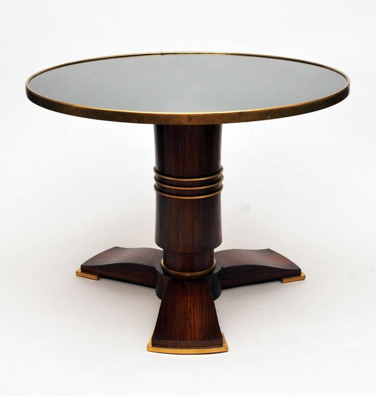French Art Deco Coffee Table by Jules Leleu (1883-1961)<br />
In mahogany wood, the tripod base with gilded bronze feet; with pedestal leg encircled by bronze rings and surmounted by a bronze trimmed antiqued mirror top, circa 1939. Model documented