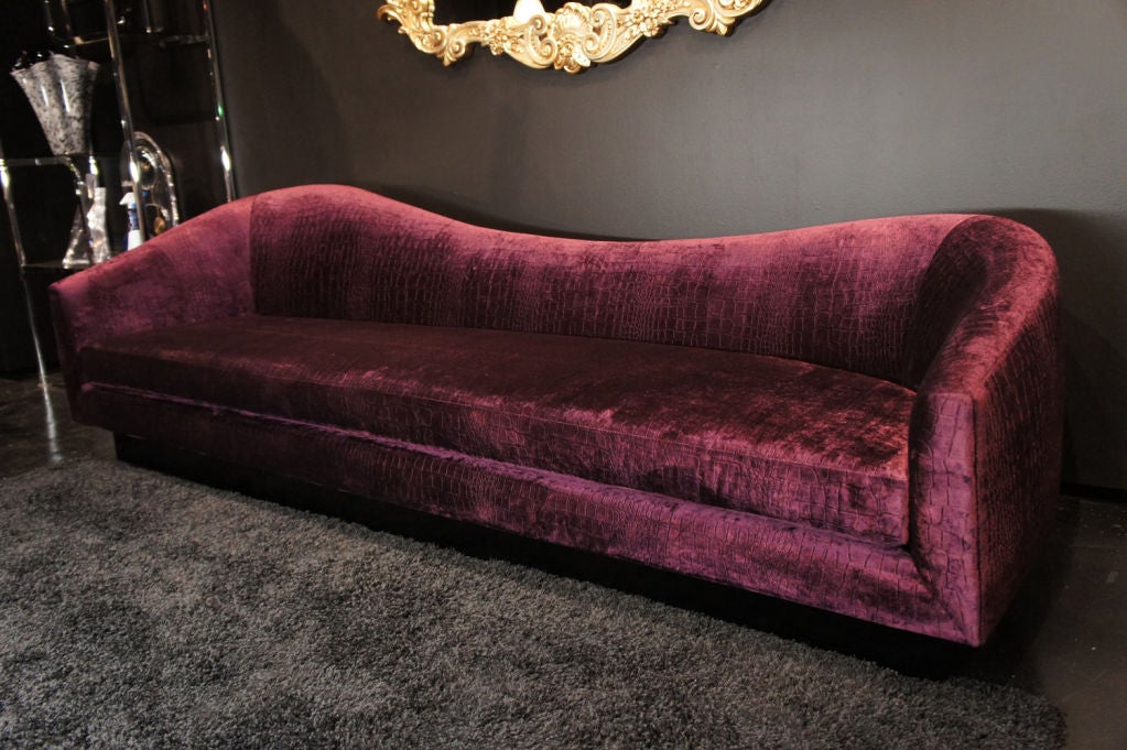 A combination of charm, sexiness and intelligence defines this extravagant sofa.  Assymetrical curves along the back also curve forward at each end, forming the arms. Upholstered in crocodile-textured aubergine velvet.  The recessed base is