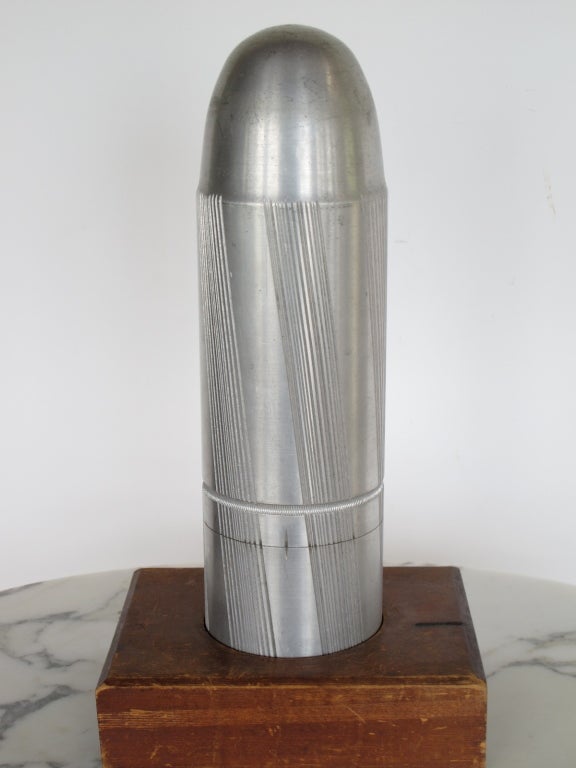 A vintage aluminum mold, bullet shaped, on a stand.