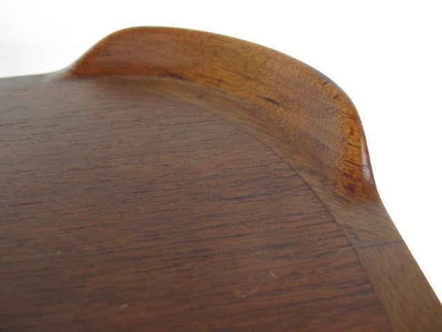 A small, square dining table in teak wood with rounded corners and raised lip edges. Finn Juhl design, executed by Baker Furniture.