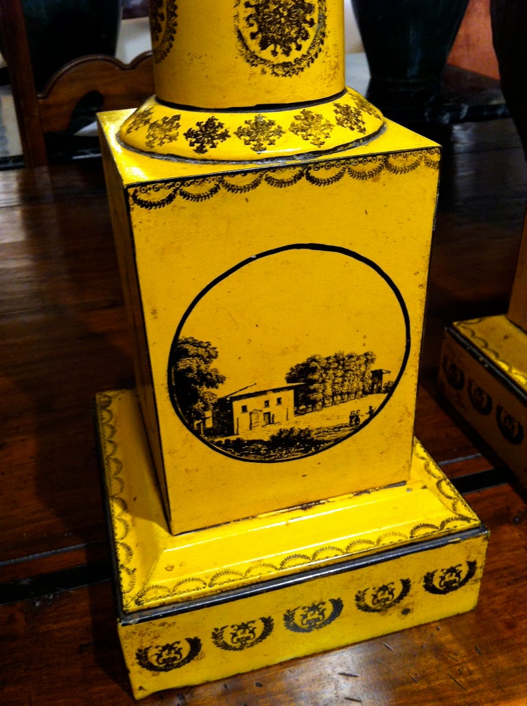 Large-scale pair of French neoclassical style column-form yellow 'tole peinte' table lamps with black stenciled scenes of the Place Vendome, Napoleonic soldiers and landscapes. This impressive pair of lamps would be great in an entry way, or any