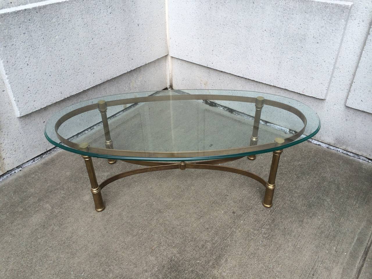Mid-Century neoclassical style brass coffee table with glass top. The base a handsome modern interpretation of the neoclassical style, with four fluted column legs joined by a curving X-stretcher with a finial in center.