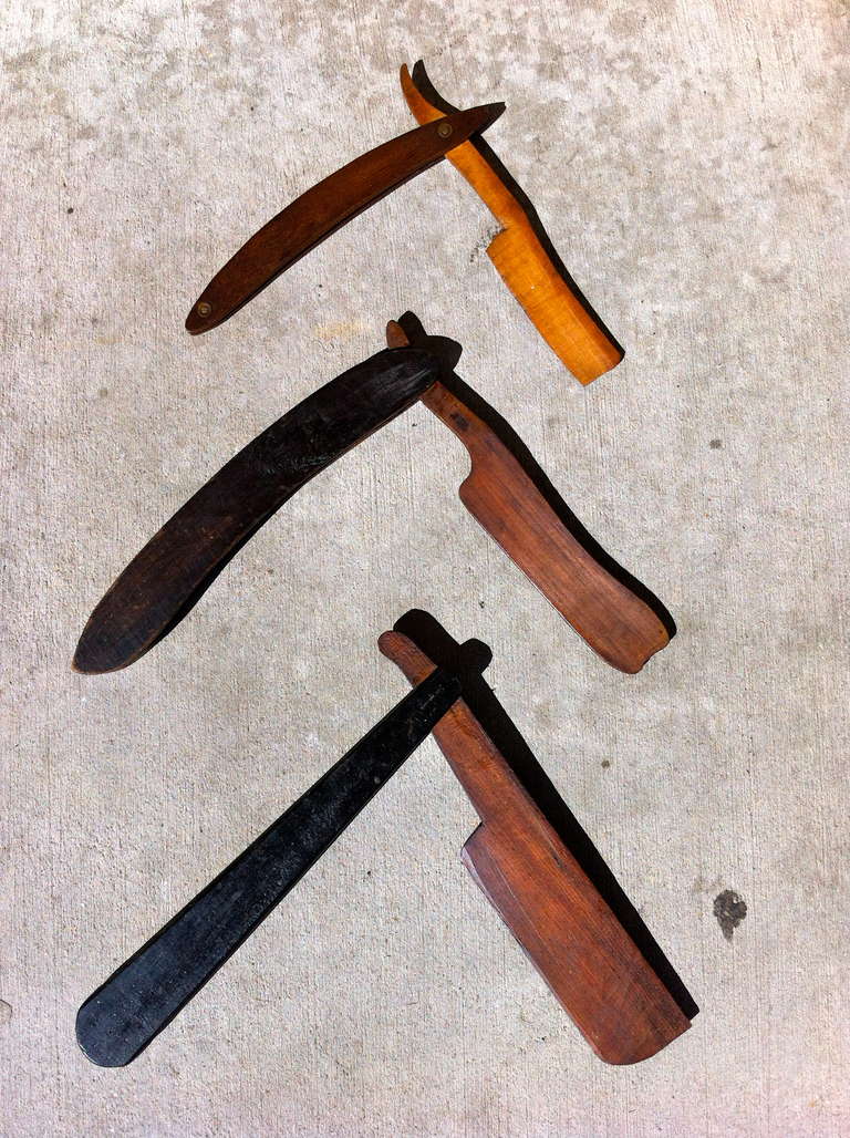 Three whimsical American folk carved wood art trade signs in the form of straight edge razors. Used by barbers as interior advertisements. Two have painted black handles, all open and close. These would be great either framed or mounted as a