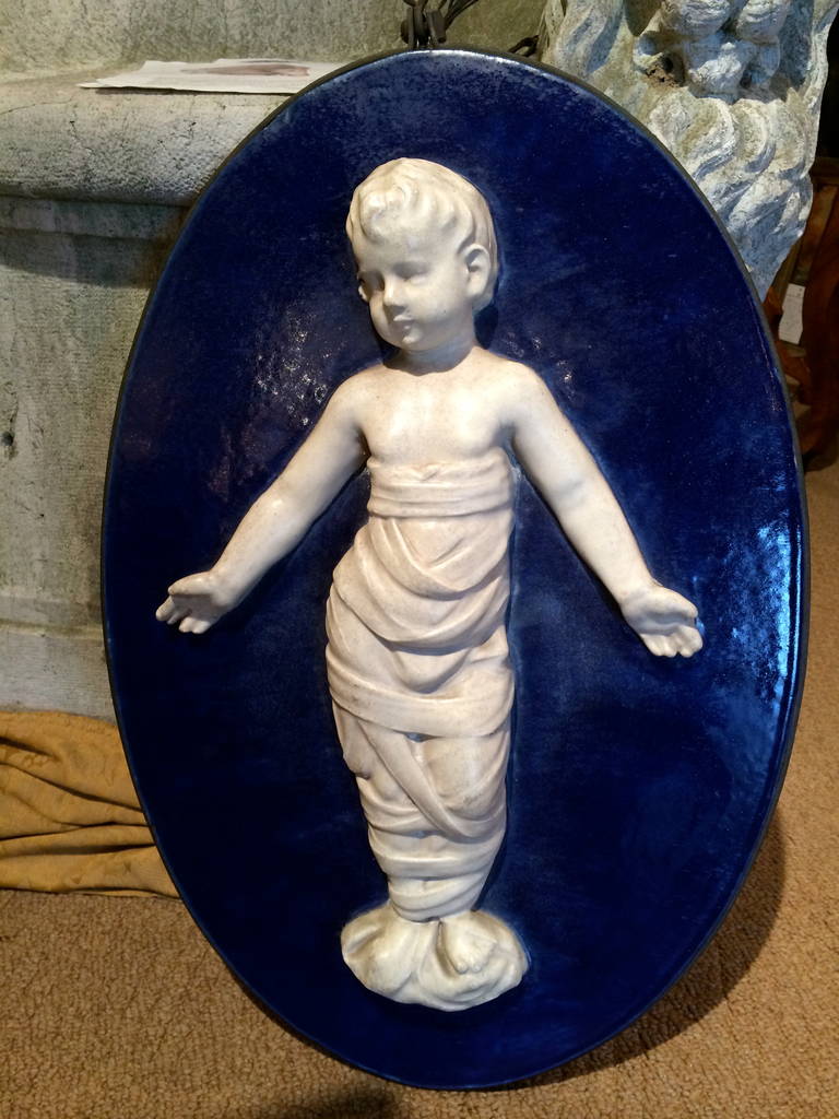 High quality Italian glazed terracotta oval plaque of a swaddled infant after the original by Renaissance artist Andrea Della Robbia. Cobalt blue background. With original wrought iron frame for hanging.

The Hospital of the Innocents in Florence