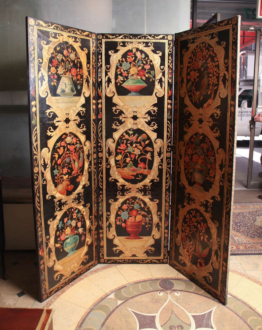 A Continental polychrome painted leather three-panel screen,  each panel with three gilt oval medallions depicting vases of flowers and exotic birds, all on a black ground. Reverse undecorated.