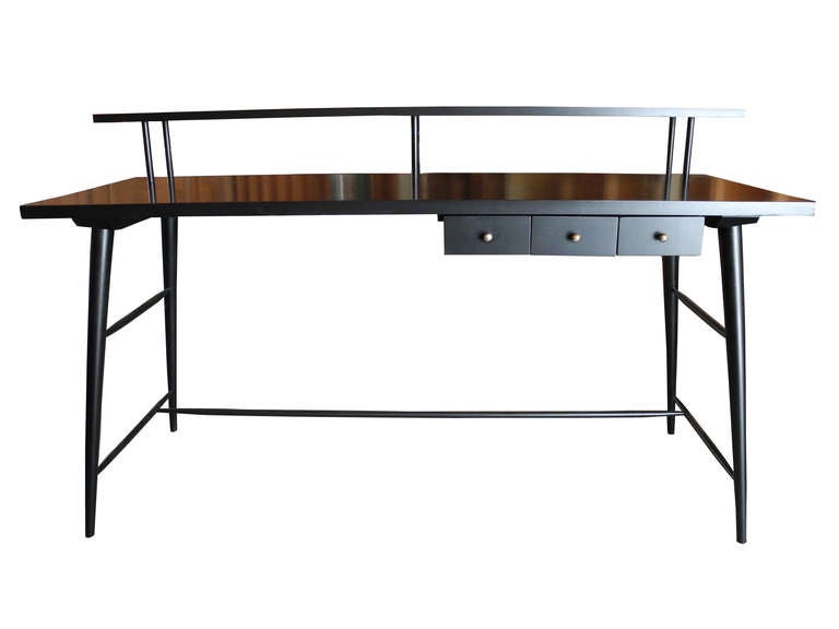 This beautiful 1950's spindle legged desk with a unique top shelf is painted and lacquered in black. It is equipped with three compartment drawers with brass handles. The surface of the desk measures 22 x 60. The surface of the shelf measures 8 x
