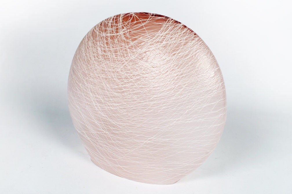 A clam-shell shape of cotton candy pink Murano glass with a merletto detail (an Italian term meaning net-like patterns of lattimo threads or opaque white glass (lattimo: from Latte, Italian for milk). A single bulb sits at the base and creates a