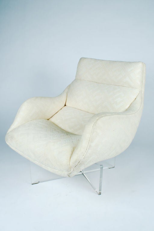 A pair of swank low slung lounge chairs with a plush seat, back and arms in a cream upholstery all raised on a swivel cross form Lucite base, which creates a floating effect.  By Vladimir Kagan. American, circa 1970.  <br />
<br />
Price is COM