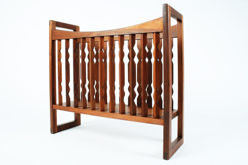 A walnut magazine stand in a crib-like form with an open frame of geometric spindles and rectangular ends that act as handles and feet, amply sized to cradle   periodicals and newspapers. By Drexel Furniture. U.S.A., circa 1960.