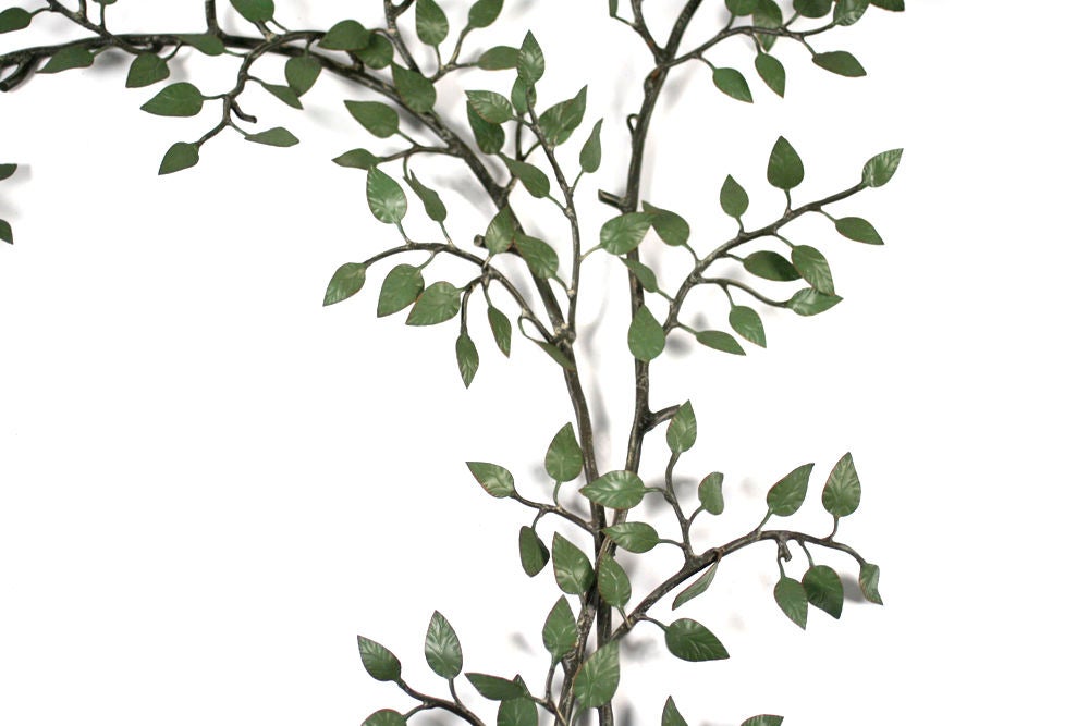 A wonderful wall mounted metal sculpture in the shape of two bending tree branches with enameled green leaves. Italian, circa 1950.