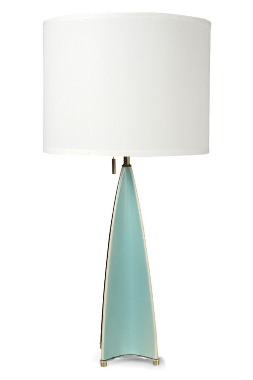 A Modernist table lamp in an elongated parabolic form with concave sides in a pattern of alternating aqua and dark grey glaze. The porcelain body raised on a brass plate base with cylindrical brass feet. By Gerald Thurston for Lightolier. U.S.A.,
