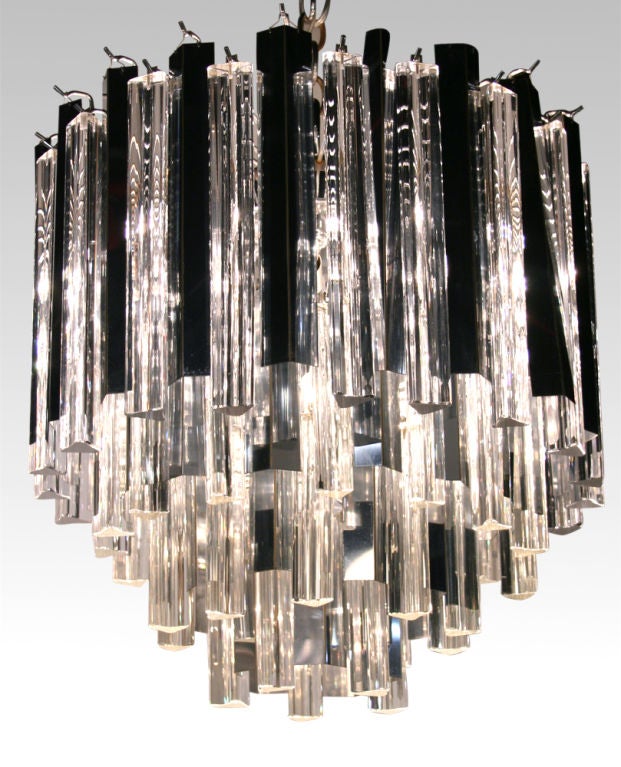 A circular chandelier comprised of alternating chromed steel fins and triangular glass rods around a four tiered metal frame.  By Camer. Italian, circa 1960.
