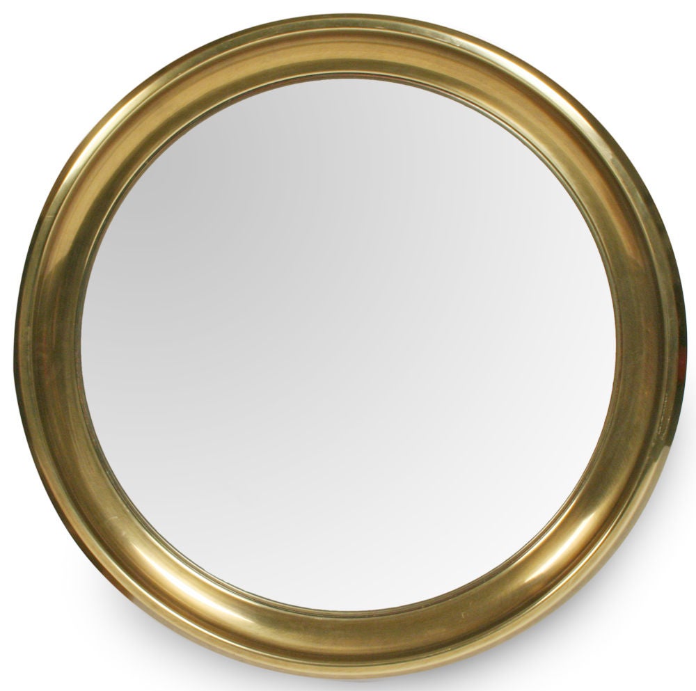 A large porthole mirror set within a wide rimmed antique brass circular frame with an attenuated interior bevel. By Mastercraft. U.S.A., circa 1970.