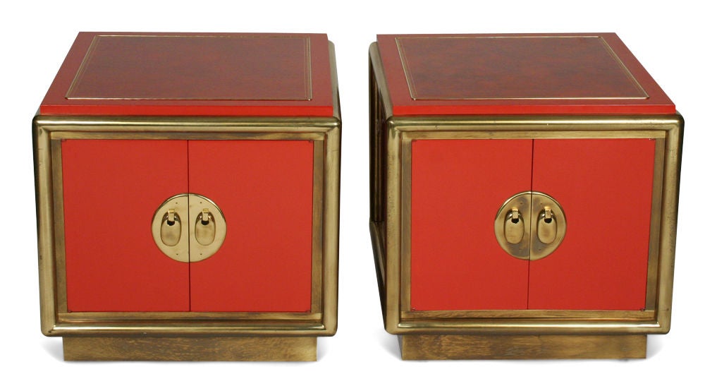 A pair of nightstands or end table cabinets in cube form comprised of inset leather tops, tubular brass frames and brass escutcheons and door pulls, finished with a cinnabar colored lacquer, all raised on brass wrapped plinth bases. By Mastercraft.