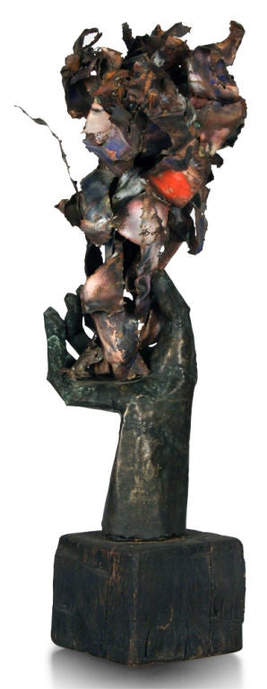 A funky brutal sculpture comprised of abstract metal flames and articulated hand all supported on a black painted wooden block base.  American, circa 1970.