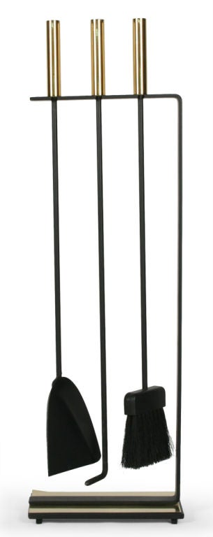 A set of fireplace tools consisting of three instruments with polished brass cylindrical handles supported by an integral freestanding rack in wrought iron with a polished brass base. Manufactured by Pilgrim. American, circa 1950.