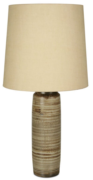 A ceramic table lamp in a cylinder form with a ribbed surface and a striated glaze in oatmeal and brown. Signed to base. By Nancy Wickham. U.S.A., circa 1950s.