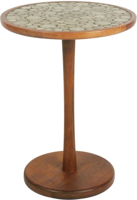 A pedestal side table with a round top inlaid with mottled taupe and brown glazed circular ceramic tiles in various diameters, the top supported by a solid turned walnut stem pedestal base. By Jane and Gordon Martz for Marshall Studios. U.S.A.,