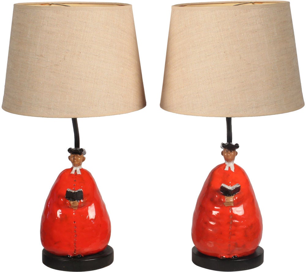 A quaint pair of ceramic table lamps each comprised of abbot figures in red, black and white glaze, with wrought iron stems and wood bases. Impressed mark [F] and script signature [FR Italy] to the base. Italy, circa 1950.