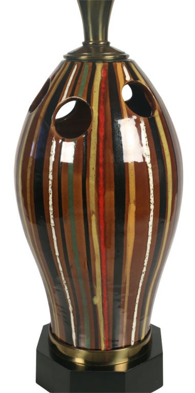 A table lamp comprising a ceramic body in a bullet form with pierced circles and hand-painted in multicolored stripes on a chocolate brown ground in a high-gloss finish all resting on an octagonal ebonized wood base. By Stiffel. U.S.A., circa 1950.