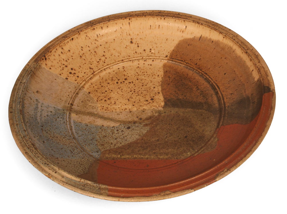 A large stoneware charger with an abstract design in brick red, brown, blue-grey and oatmeal colors with a speckled finish. Artist signature to the base [John Nickerson]. circa 1970.