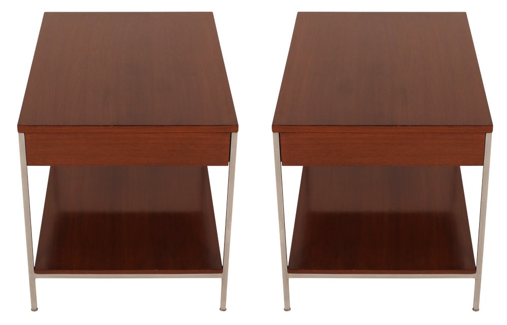 A Modernist pair of end tables each comprising a walnut top with a single drawer and a lower shelf all within a satin steel frame. Retains manufacturer's tag. By George Nelson for Herman Miller. U.S.A., circa 1950. [DUF0307A] [DUF0307B]