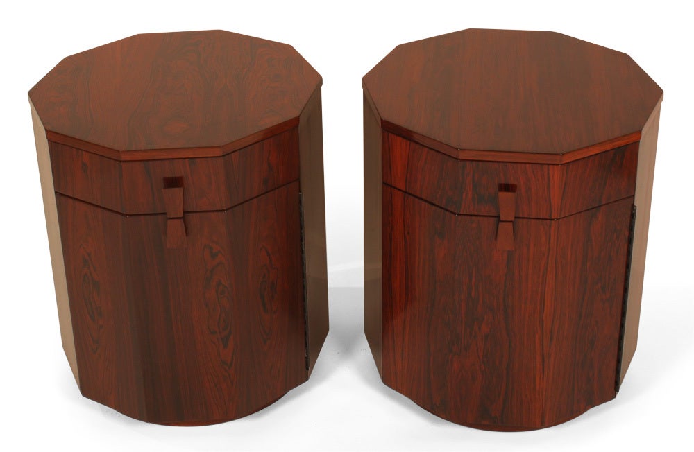 A beautiful pair of ten sided cabinets or dry bars in Rosewood comprising trapezoidal wood pulls, upper drawer above a door compartment all supported on a round wood plinth. Door incorporates two shelves for storing bottles. Designed and produced by