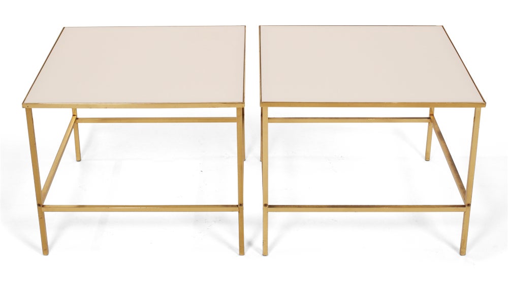 A pair of side tables in a square form with white inset Vitrolite glass tops on polished solid brass frames. After Harvey Probber. U.S.A., circa 1950.